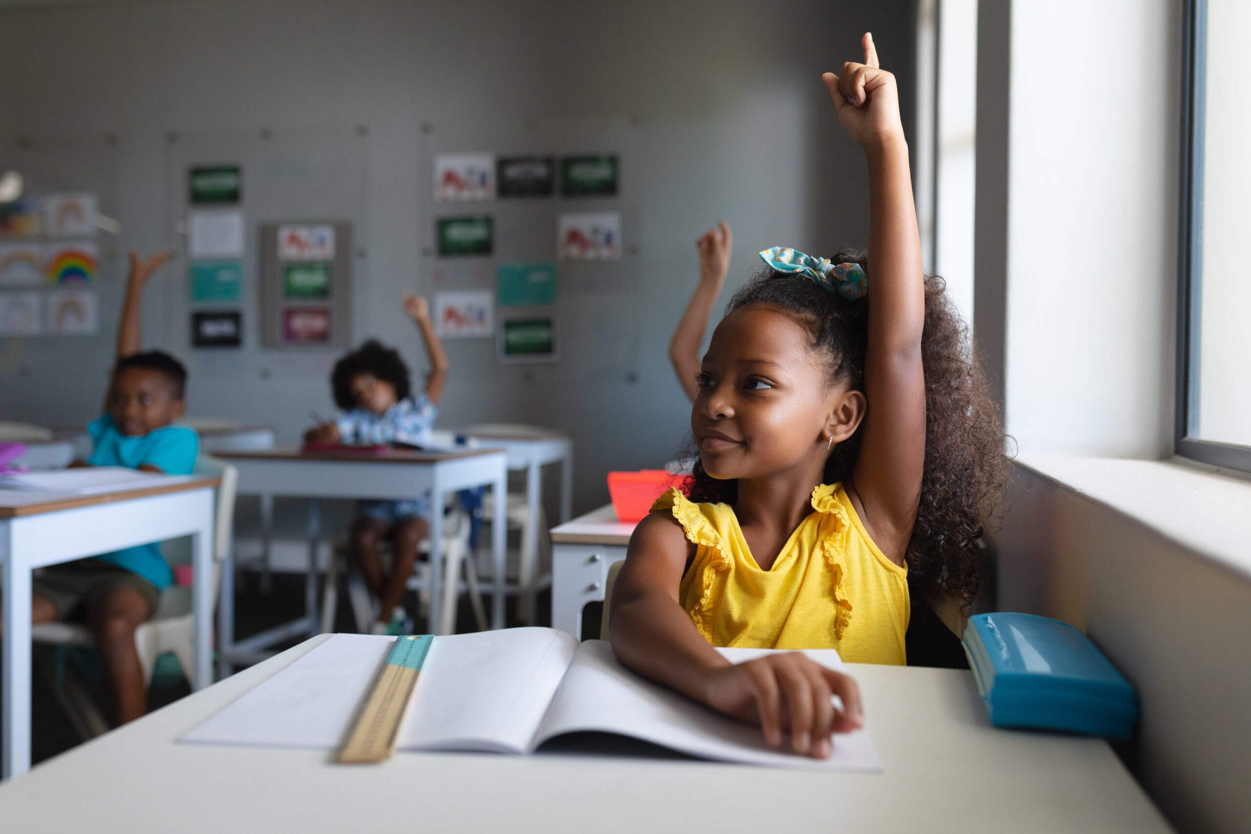 des eleves d ecole elementaire afro americains avec les mains levees assis a un bureau en classe scaled