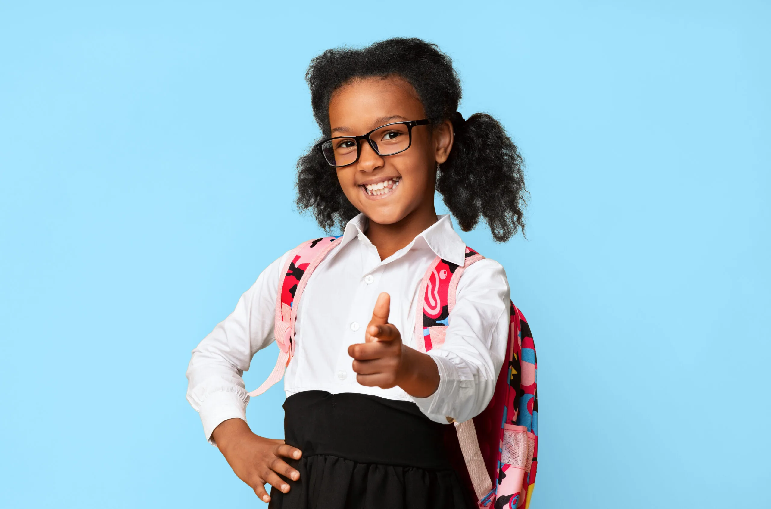 une ecoliere afro americaine heureuse montrant du doigt la camera en studio scaled